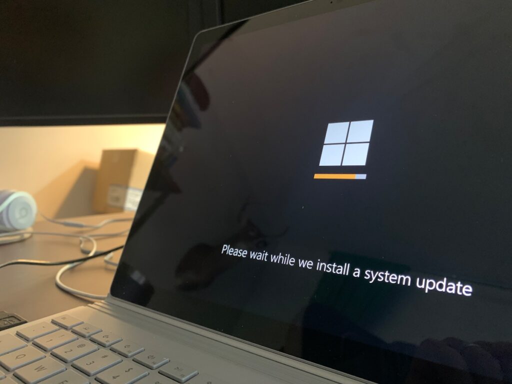 Laptop screen displaying a Windows update screen with a small orange progress bar and the message 'Please wait while we install a system update'