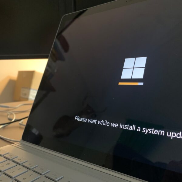Laptop screen displaying a Windows update screen with a small orange progress bar and the message 'Please wait while we install a system update'