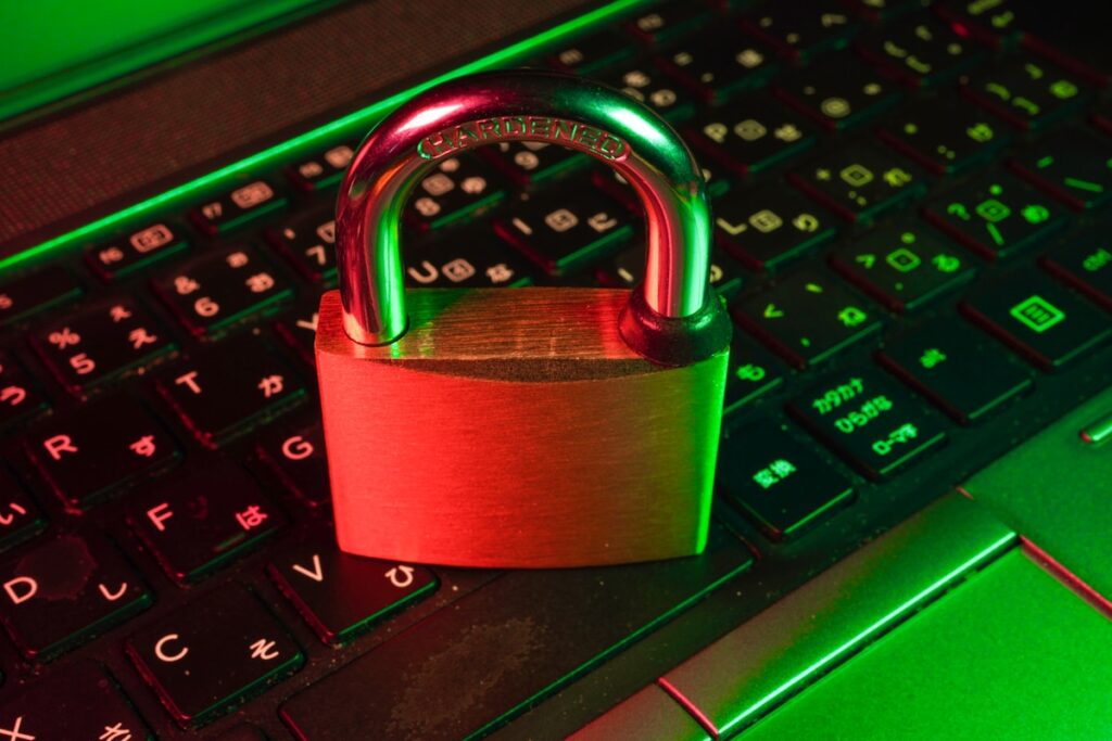 Padlock resting on a laptop keyboard under red and green lighting, symbolizing cybersecurity and data protection