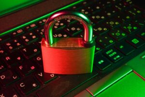 Padlock resting on a laptop keyboard under red and green lighting, symbolizing cybersecurity and data protection