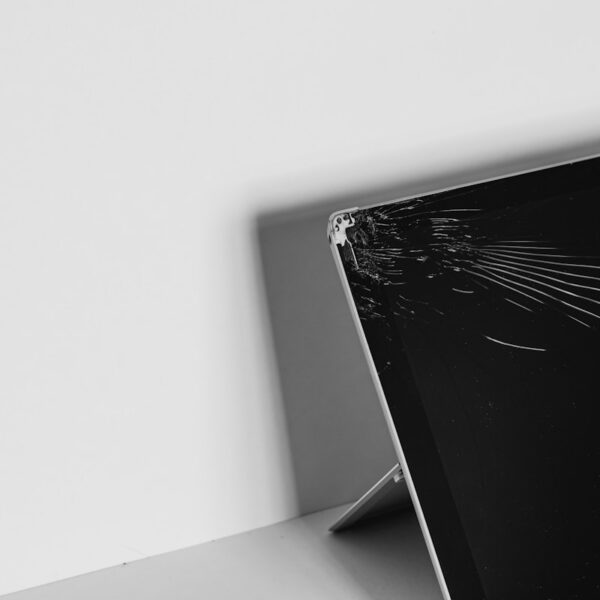 Black-and-white photo of a laptop with a cracked screen propped up on a desk edge.